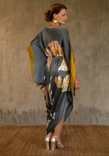 Load image into Gallery viewer, Back detail: asymmetric long dress in grey steel background and floral pattern in pink and gold. Deep gold border on the kimono-like sleeves.Luxury resort-wear in silk batik made in Bali. 
