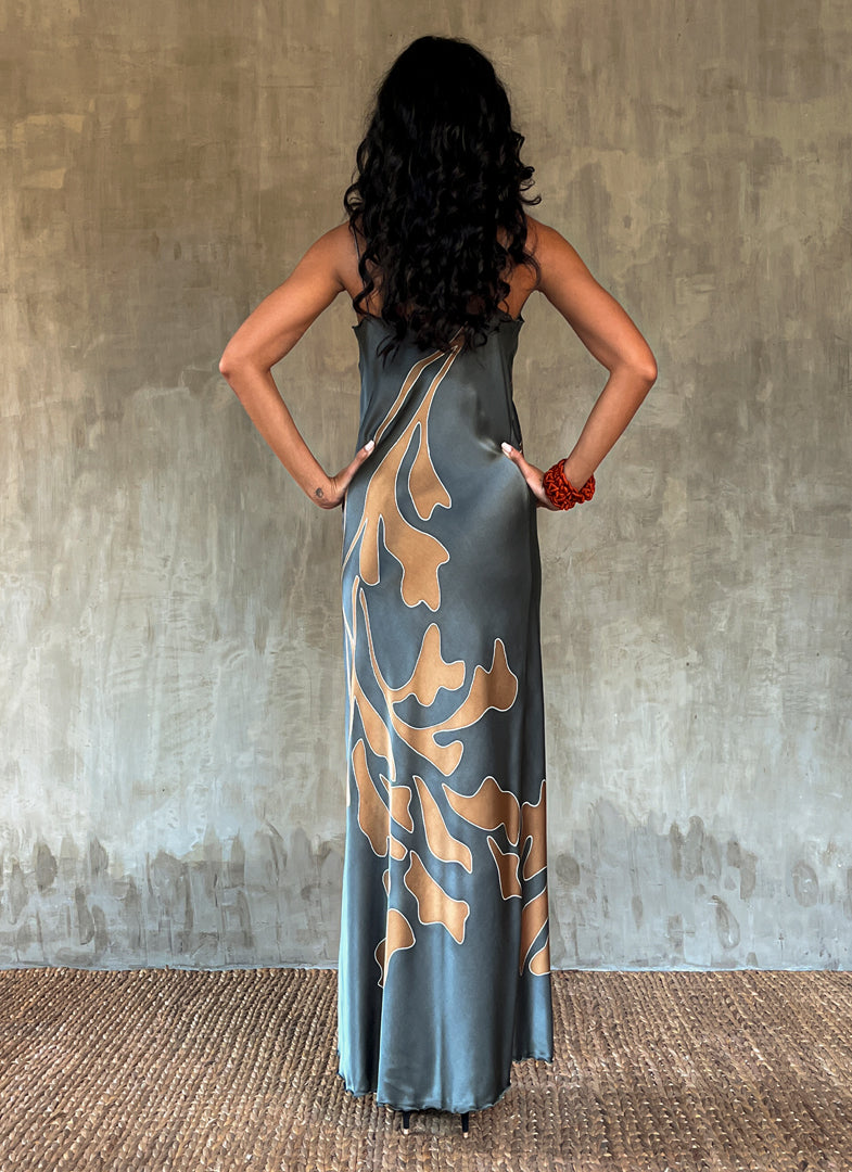 Back detail: Silk satin handcrafted bias long spaghetti dress in steel grey with maxi foliage pattern front and back. Bias cut dress with low V-neckline.