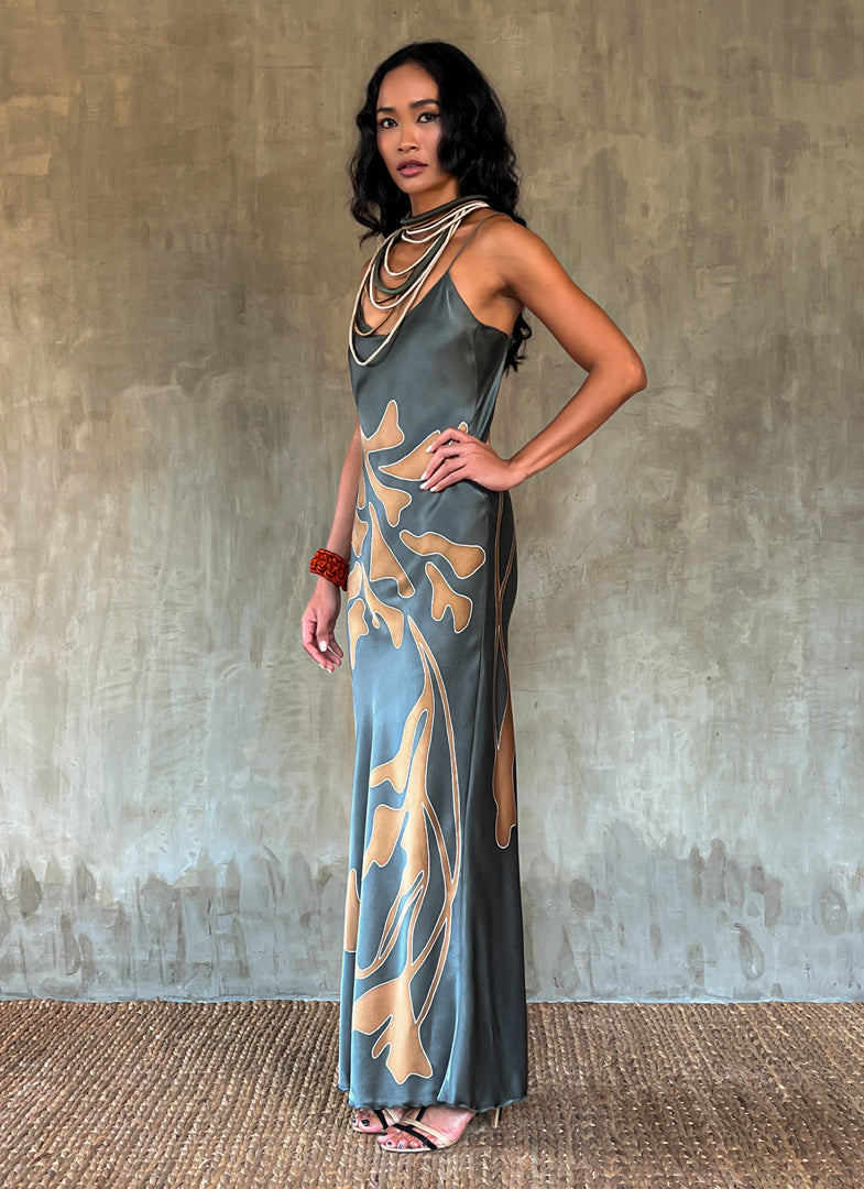 Side detail: silk satin handcrafted bias long spaghetti dress in steel grey with maxi foliage pattern front and back. Bias cut dress with low V-neckline.