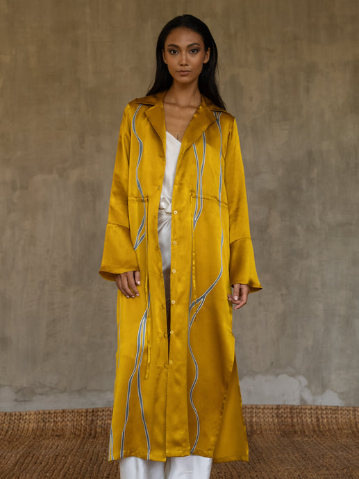 Quarzia hand-crafted in glossy pure silk, this jacket' neck-line dress it has elegant, structured trumpet cuffs,   discreet pockets and waist drawstring add to the sophistication and comfort. The stunning gold colour is set-off by the contemporary hand-painted Kintsugi design, inspired by the Japanese technique for broken ceramics.