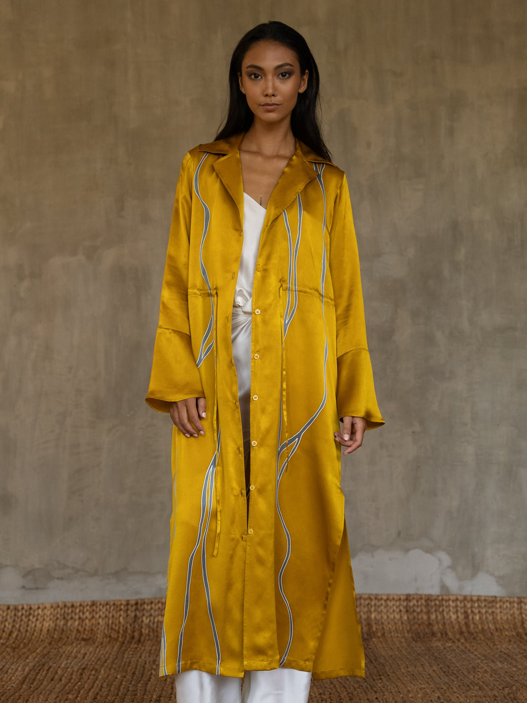Quarzia hand-crafted in glossy pure silk, this jacket' neck-line dress it has elegant, structured trumpet cuffs,   discreet pockets and waist drawstring add to the sophistication and comfort. The stunning gold colour is set-off by the contemporary hand-painted Kintsugi design, inspired by the Japanese technique for broken ceramics.