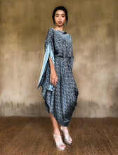 Load image into Gallery viewer, Asymmetric long Jogya silk dress with a &quot;Deco&quot; pattern in grey and dark blue colors. The dress features a loose fit with a belt and has a subtle asymmetrical design. Steel grey border define the kimono-like sleeves. Luxury resort-wear in silk batik made in Bali. 
