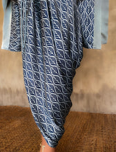 Load image into Gallery viewer, Detail of pattern &quot;Deco&quot; in grey and blue color on Jogya Dress in silk satin. The dress features a loose fit with a belt and has a subtle asymmetrical design. Steel grey border define the kimono-like sleeves. Luxury resort-wear in silk batik made in Bali. 
