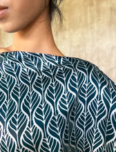Load image into Gallery viewer,  Detail of slash neck-line. Asymmetric long Jogya silk dress with a &quot;Deco&quot; pattern in grey and dark blue colors. The dress features a loose fit with a belt and has a subtle asymmetrical design. Steel grey border define the kimono-like sleeves. Luxury resort-wear in silk batik made in Bali. 
