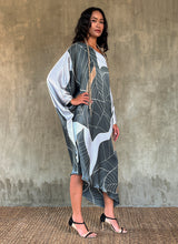 Load image into Gallery viewer, Side- detail: Silk satin handpainted asymmetric long dress in Greenwall botanical pattern in light blue background and darker leaves .

