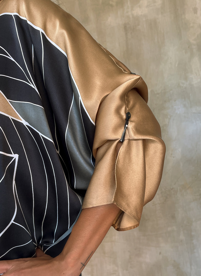 Detail of 3/4-length split sleeves. One sleeve can be adjusted to two different lengths with a discreet button-and-loop fastening —Silk satin handpainted asymmetric long dress in Greenwall botanical pattern in gold background and darker leaves .