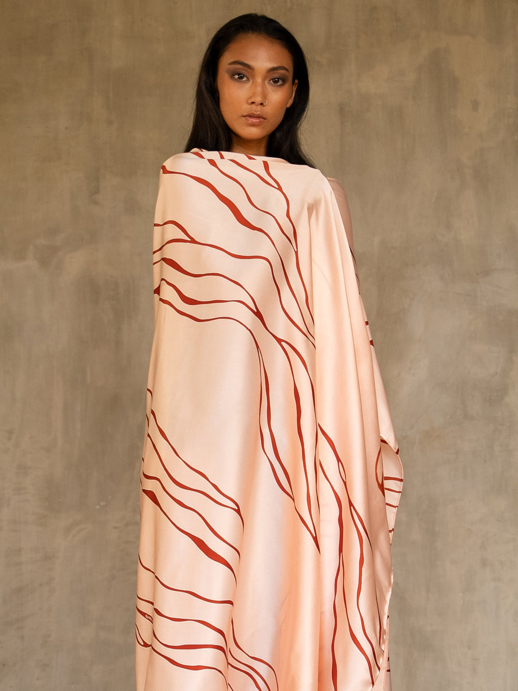 A woman wearing a pink champagne colored silk sarong batik with a geometric kintsugi pattern, tied in a knot at the waist. Handmade in Bali