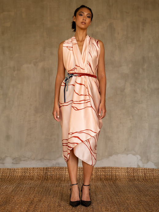 A woman wearing a pink champagne colored silk sarong with a geometric kintsugi pattern, tied in a knot at the waist, standing against a textured background.