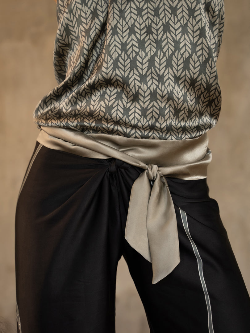 A female model wearing a steel grey satin silk halter top with a geometric leaf batik pattern and a matching silk long pant black with a grey lines motif produced in Bali