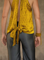 A female model wearing a satin silk halter top with a geometric leaf batik pattern in gold yellow and yellow color and a matching silk long pant grey with lines yellow motif produced in Bali